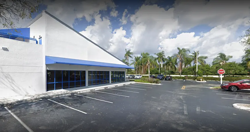 Pines-200 Commercial building with a blue awning and an empty parking lot, surrounded by palm trees.